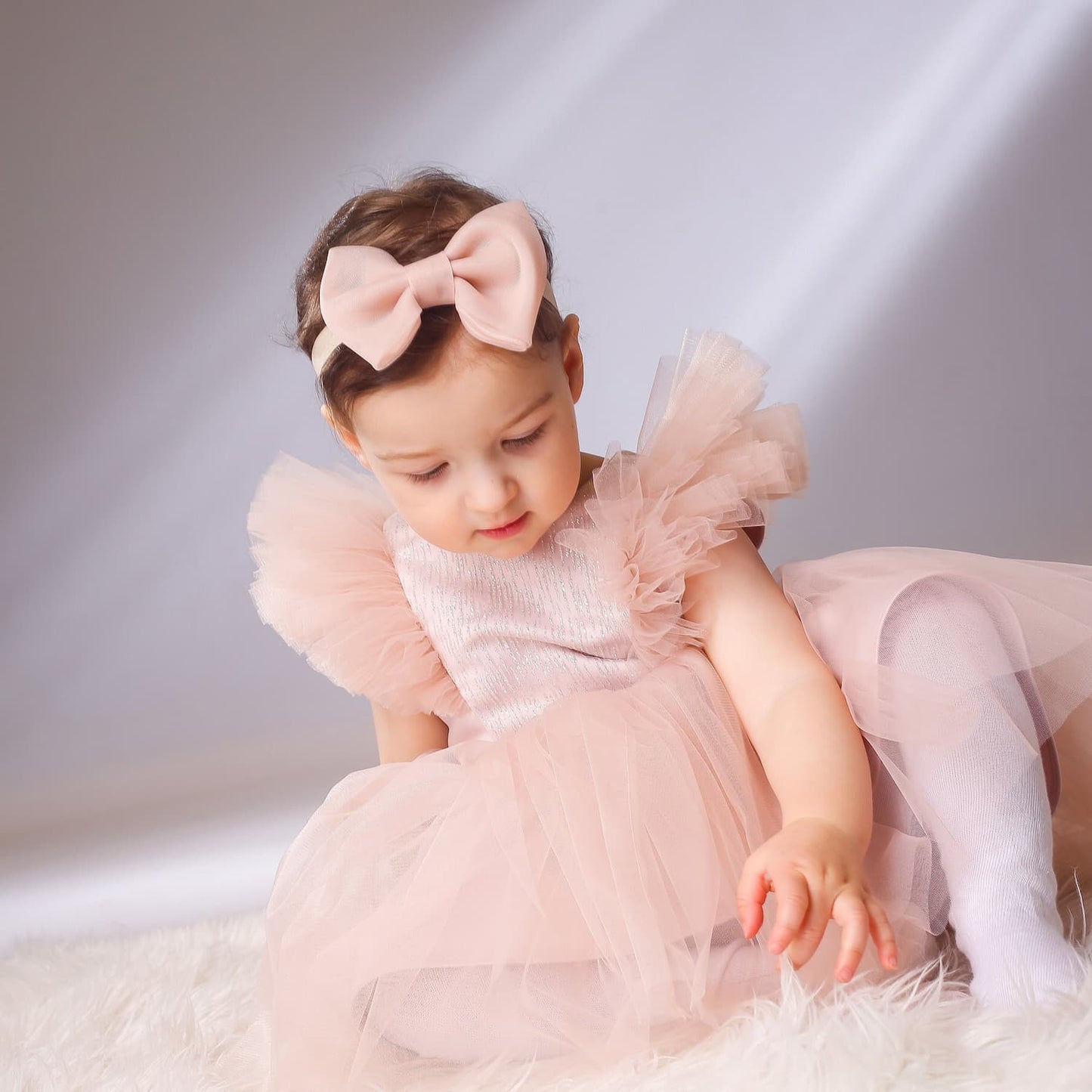 Girl wearing blush pink flower girl dress with matching tulle hair bow – elegant festive outfit for special occasions