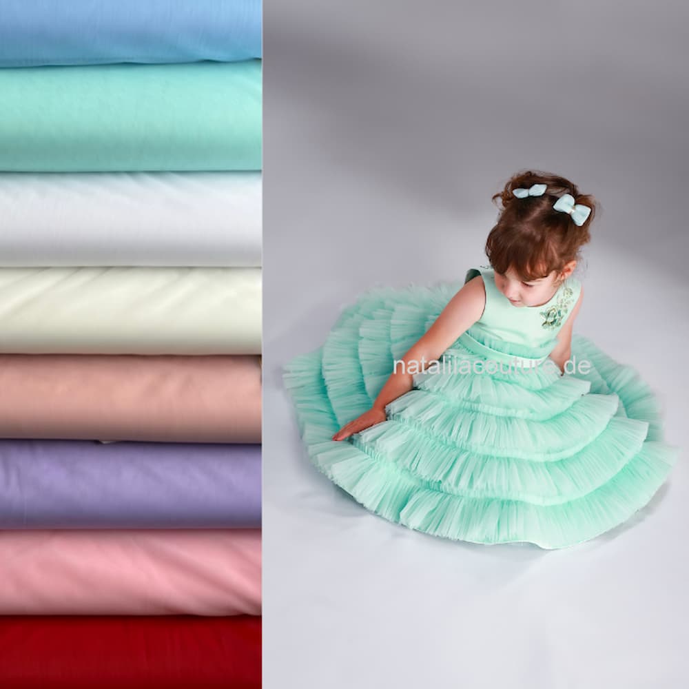 Modell in festlichem Tüllkleid in Mintfarbe neben einer Auswahl an Tüllstoffen in verschiedenen Farben für individuelle Mädchenkleider zur Bestellanfertigung